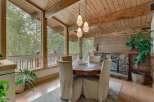 Experience cozy dining with a view in this charming space, featuring a rustic round dining table and chairs set against a backdrop of large windows overlooking a serene forest.