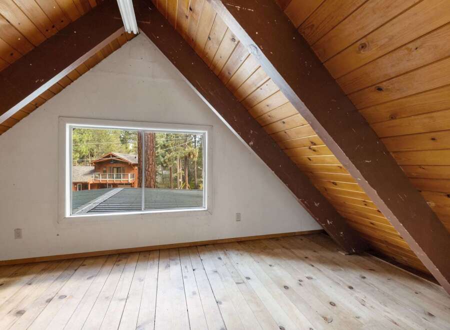 Discover the potential of this charming attic space, featuring exposed wooden beams and a large window offering scenic views.
