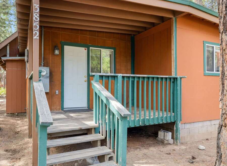 Charming cabin entrance featuring a welcoming wooden porch with a vibrant teal railing and stairs leading up to a classic white door.