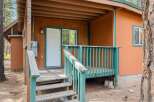 Charming cabin entrance featuring a welcoming wooden porch with a vibrant teal railing and stairs leading up to a classic white door.