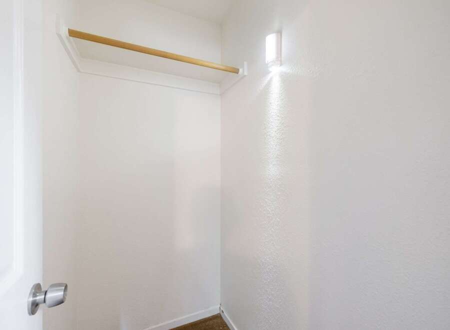 Discover ample storage in this spacious walk-in closet, featuring a sturdy wooden rod for hanging clothes and a bright overhead light to illuminate your wardrobe.