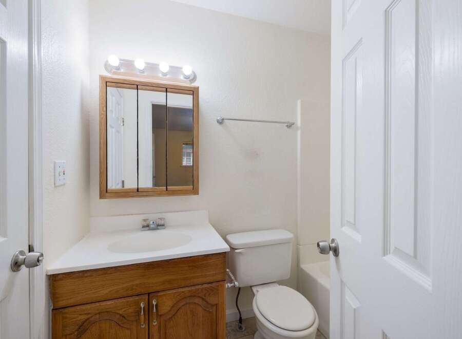 This bathroom features a spacious vanity with ample storage, a bright mirror with overhead lighting, and a clean white toilet.