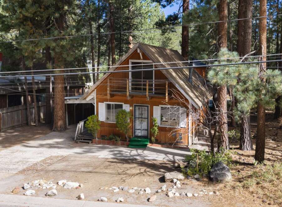 Nestled amongst tall pine trees, this charming cabin offers a rustic retreat with its warm wood exterior and inviting porch.