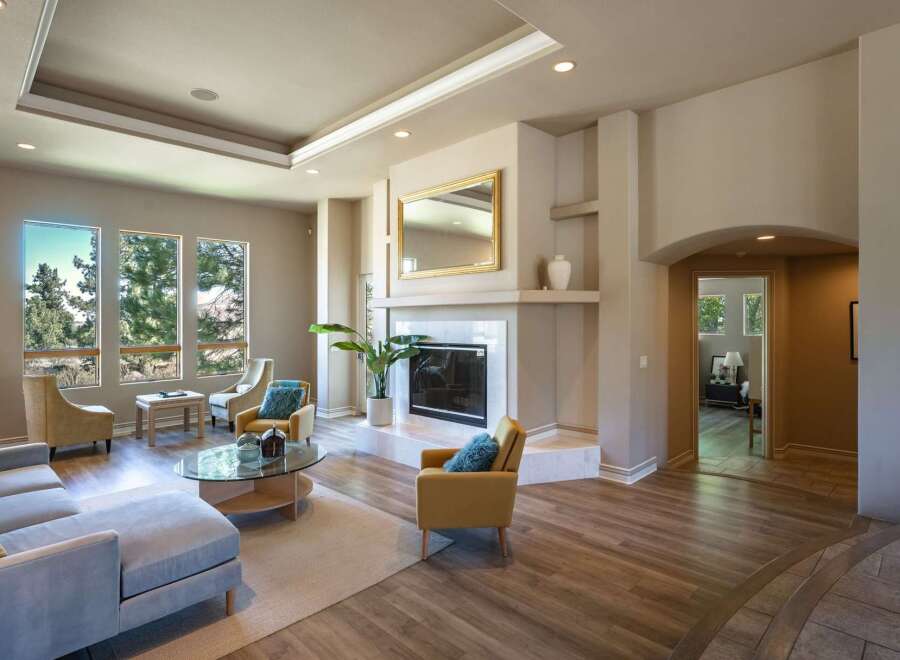 Step into this inviting living room, featuring a cozy fireplace with a decorative mirror above and ample natural light from large windows.
