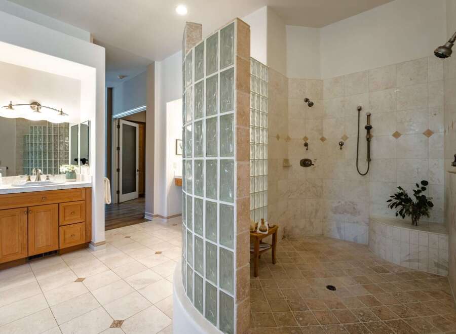 Experience luxury in this spacious master bathroom, featuring a stunning walk-in shower enclosed by a curved glass block wall.