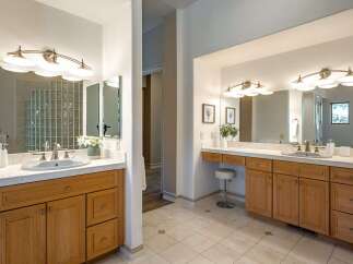 This spacious bathroom features dual vanities with ample counter space and warm wooden cabinetry, perfect for a master suite.