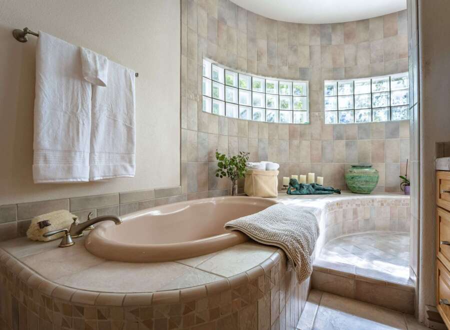 Indulge in relaxation in this luxurious bathroom featuring a spacious corner bathtub with a tiled surround and a separate shower area.