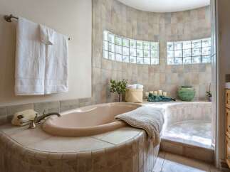 Indulge in relaxation in this luxurious bathroom featuring a spacious corner bathtub with a tiled surround and a separate shower area.