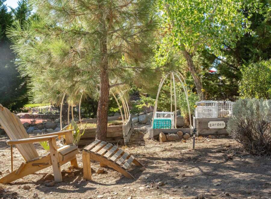 Enjoy the outdoors in this charming garden space featuring comfortable Adirondack chairs and a unique wooden footrest, perfect for relaxing.