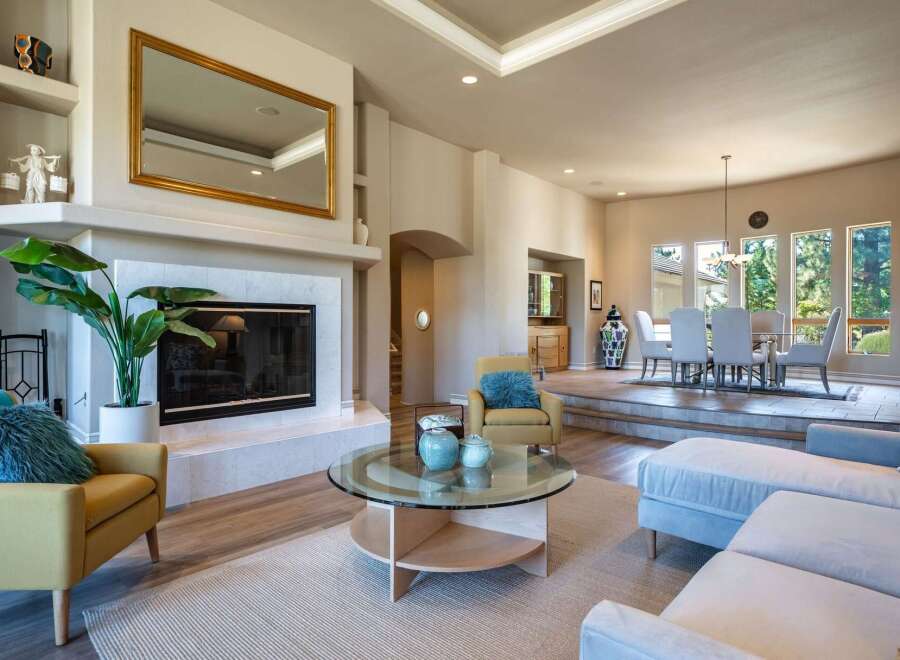 This spacious living area boasts a modern fireplace with a large gold-framed mirror above, complemented by a cozy yellow armchair and a plush blue accent pillow.