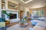 This spacious living area boasts a modern fireplace with a large gold-framed mirror above, complemented by a cozy yellow armchair and a plush blue accent pillow.