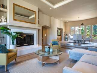 This spacious living area boasts a modern fireplace with a large gold-framed mirror above, complemented by a cozy yellow armchair and a plush blue accent pillow.