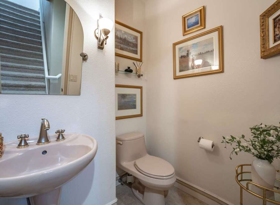 This powder room features a stylish pedestal sink with brushed nickel fixtures, complemented by a large arched mirror reflecting a carpeted staircase.