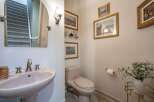 This powder room features a stylish pedestal sink with brushed nickel fixtures, complemented by a large arched mirror reflecting a carpeted staircase.