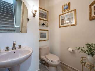 This powder room features a stylish pedestal sink with brushed nickel fixtures, complemented by a large arched mirror reflecting a carpeted staircase.