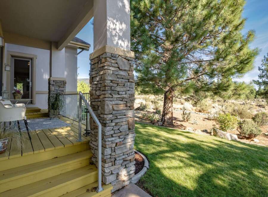 Welcome guests onto a charming yellow-painted porch with a stone-accented pillar, perfect for enjoying the serene natural surroundings.