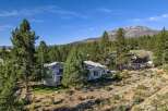 Nestled amidst towering pine trees and offering breathtaking mountain views, this stunning property boasts a modern white home with multiple balconies and a lush green lawn.