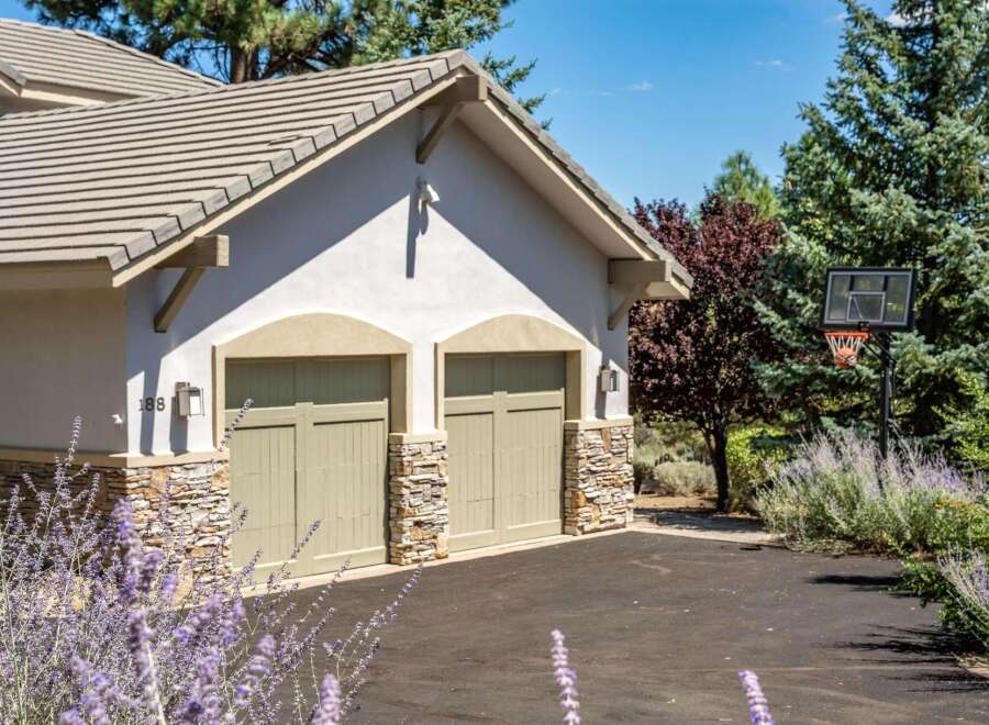 This charming property features a two-car garage with attractive stone accents and light green doors, complemented by a light-colored stucco exterior.