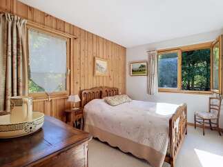 This charming bedroom features warm wood-paneled walls and a cozy queen-sized bed adorned with a delicate floral quilt.