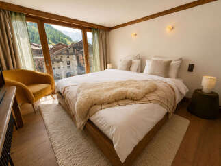 Experience breathtaking mountain views from this luxurious bedroom, featuring a cozy armchair and a plush sheepskin throw on the bed.