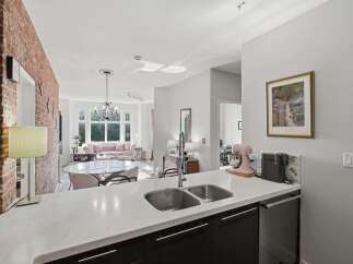 Experience modern living in this open-concept condo, featuring a stunning brick accent wall and a sleek kitchen with a double sink and stainless steel appliances.