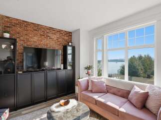 Experience breathtaking waterfront living in this stunning living room, featuring a chic pink velvet sofa and a dramatic exposed brick accent wall.