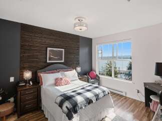 Experience serene waterfront living in this beautifully appointed bedroom, featuring a striking wood-slat accent wall and a large window offering picturesque views.