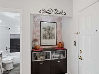 This entryway features a decorative wall accent above a dark wood cabinet displaying elegant dishware.