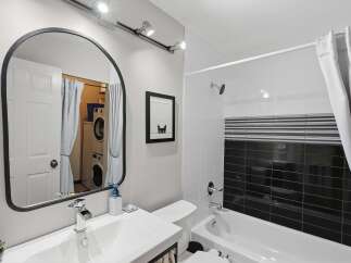 This modern bathroom features a sleek vanity with a chrome waterfall faucet and a large arched mirror reflecting a stacked washer and dryer.