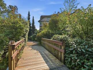 Discover this charming property featuring a picturesque wooden bridge leading to a paved walkway, surrounded by lush greenery and mature trees.