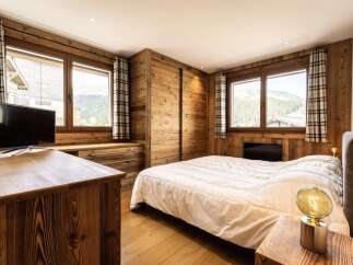 Experience rustic charm in this cozy mountain bedroom, featuring warm wood paneling and large windows with stunning forest views.