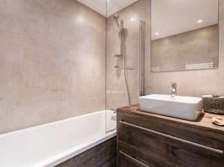 This modern bathroom features a sleek white bathtub with a glass shower screen, complemented by large, neutral-toned tiles on the walls.