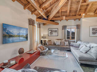 Experience luxury mountain living in this stunning chalet living room, featuring a large sectional sofa perfect for cozy evenings and a modern entertainment center with a breathtaking landscape view.