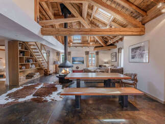 Experience rustic luxury in this stunning mountain chalet featuring a grand open-plan living area with exposed wooden beams and a striking suspended fireplace.
