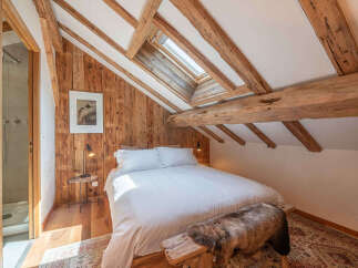 Experience rustic charm in this attic bedroom, featuring exposed wooden beams and a cozy sloped ceiling with a skylight.
