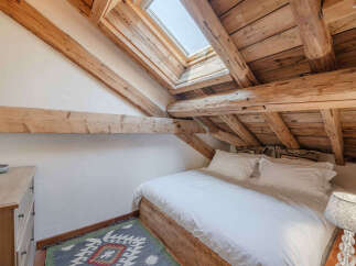 Experience rustic charm in this cozy attic bedroom, featuring exposed wooden beams and a skylight that floods the space with natural light.