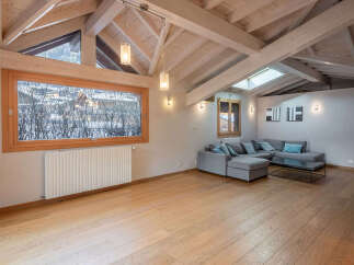 Experience luxurious living in this stunning attic apartment, featuring a spacious living area with a modern sectional sofa and a large wooden-framed window offering picturesque views.