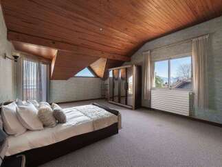 Experience cozy living in this charming attic bedroom, featuring a sloped wooden ceiling and a comfortable bed adorned with plush pillows.