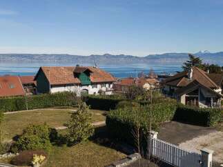 Experience breathtaking lake and mountain views from this stunning property, featuring a charming house with a classic tiled roof and lush green surroundings.