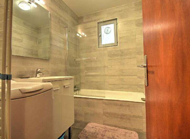 This modern bathroom features a sleek vanity with a built-in sink and ample storage, complemented by a spacious bathtub and a convenient washing machine.