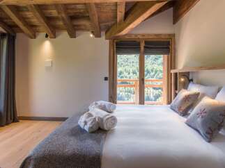 Experience ultimate comfort in this charming bedroom, featuring a plush king-sized bed adorned with decorative pillows and soft, rolled towels.