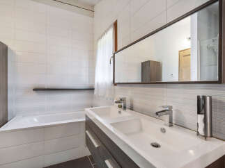 This modern bathroom features a sleek double vanity with chrome fixtures, complemented by a spacious bathtub.