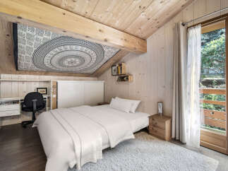 Discover this charming attic bedroom featuring a cozy bed, a functional desk area, and a unique mandala tapestry adorning the sloped ceiling.