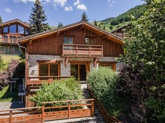 Experience alpine living in this charming wooden chalet, featuring a stone facade and multiple balconies perfect for enjoying mountain views.