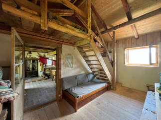 Discover this charming rustic cabin featuring a cozy living area with a comfortable sofa and a wooden staircase leading to the upper level.