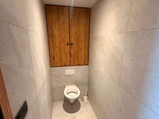 Discover this modern bathroom featuring a sleek toilet and a unique wooden cabinet for ample storage.