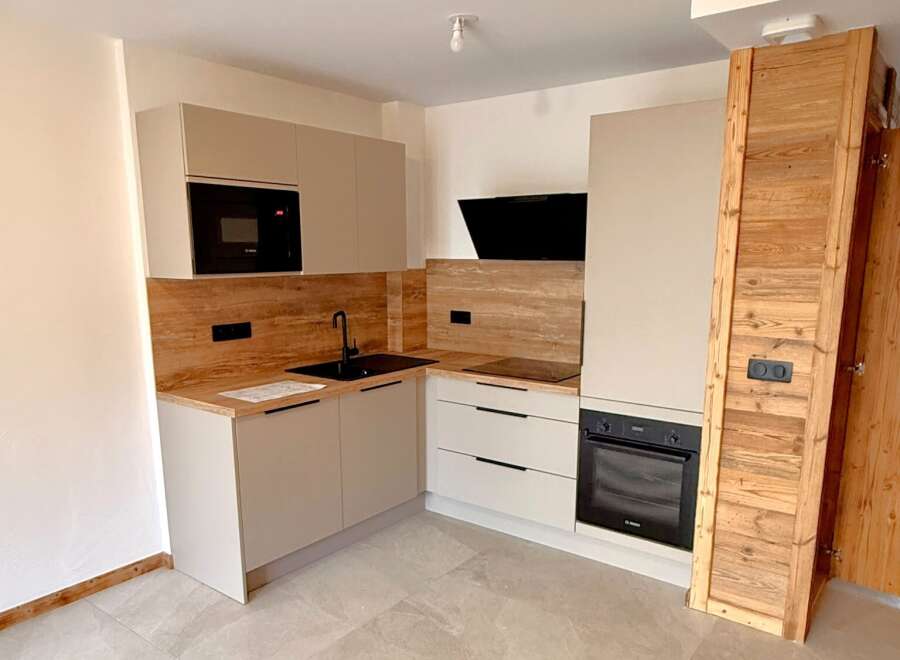 Discover this modern L-shaped kitchen featuring sleek, light-colored cabinetry and a wood-effect backsplash.