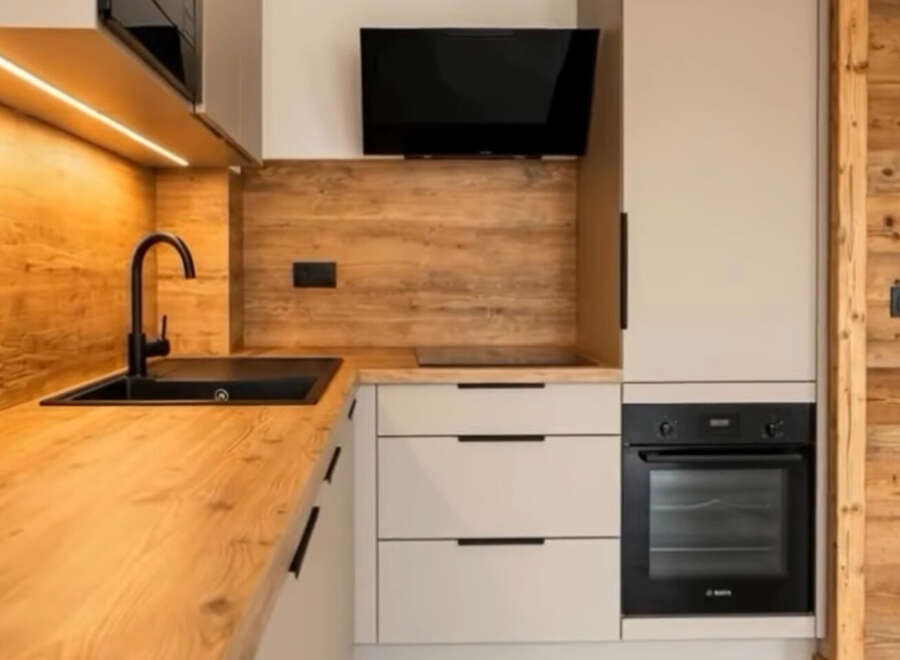 Discover this modern kitchen featuring a sleek black sink and faucet, complemented by warm wooden countertops and backsplash.