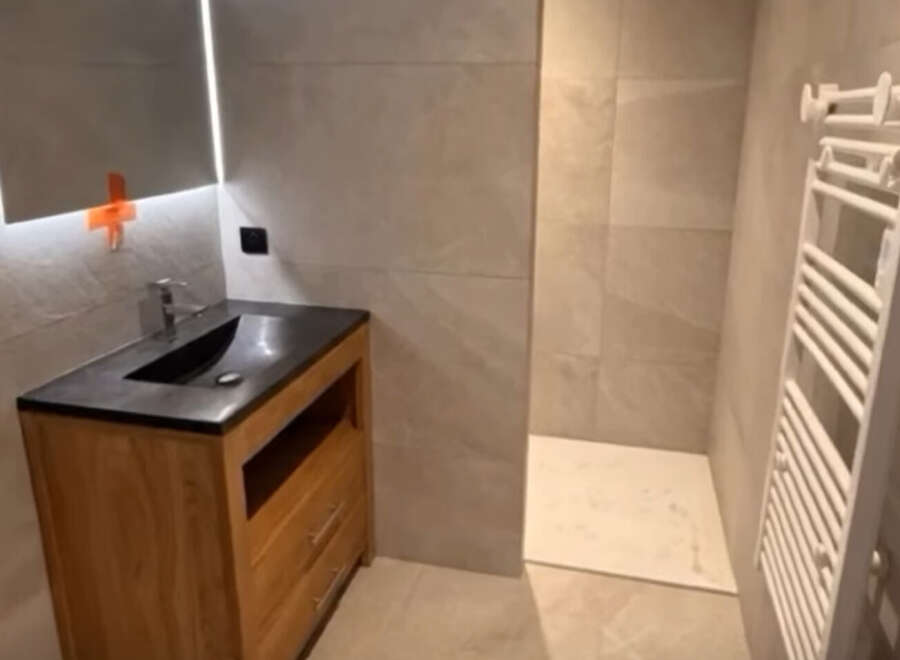 This modern bathroom features a sleek vanity with a dark countertop and a wooden cabinet, complemented by a large illuminated mirror.