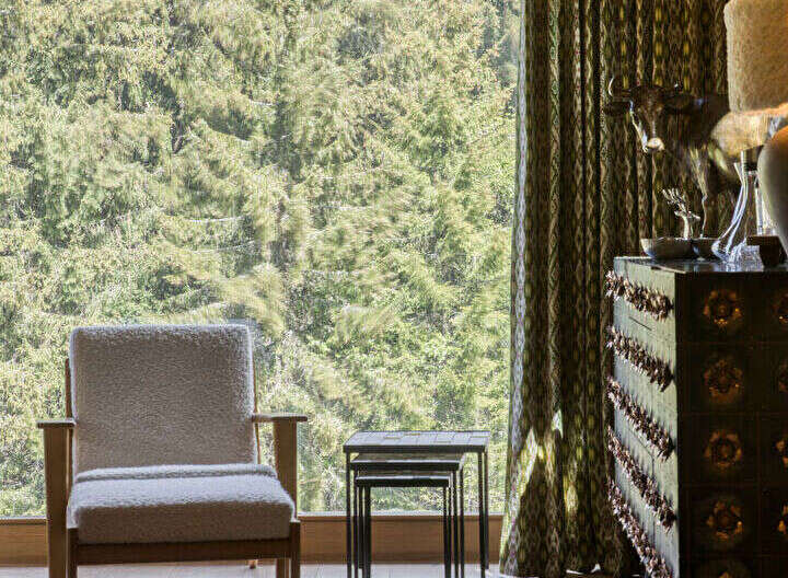 Experience rustic charm with this cozy armchair positioned by a large window overlooking a lush forest.